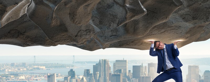 businessman holding up heavy rock in front of cityscape_canstockphoto50713044 800x315